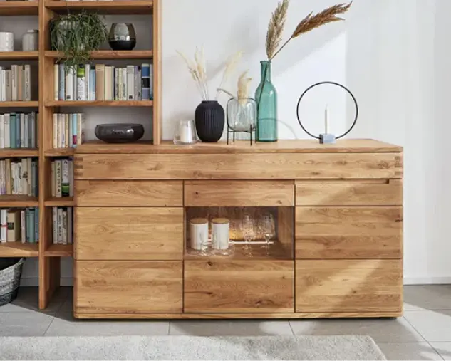 Hochwertiges Sideboard aus Massivholz mit integrierter Glasvitrine und dekorativen Vasen. Daneben ein Bücherregal aus Holz. Moderne Wohnmöbel in natürlicher Holzoptik für stilvolle und langlebige Wohnzimmer Einrichtung.